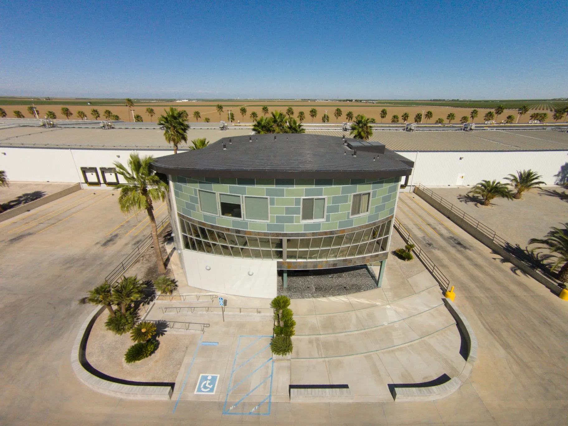 STAMOULES PRODUCE CO., INC. Aerial view of the curved green tiled office building, warehouse roof, and surrounding farmland.
