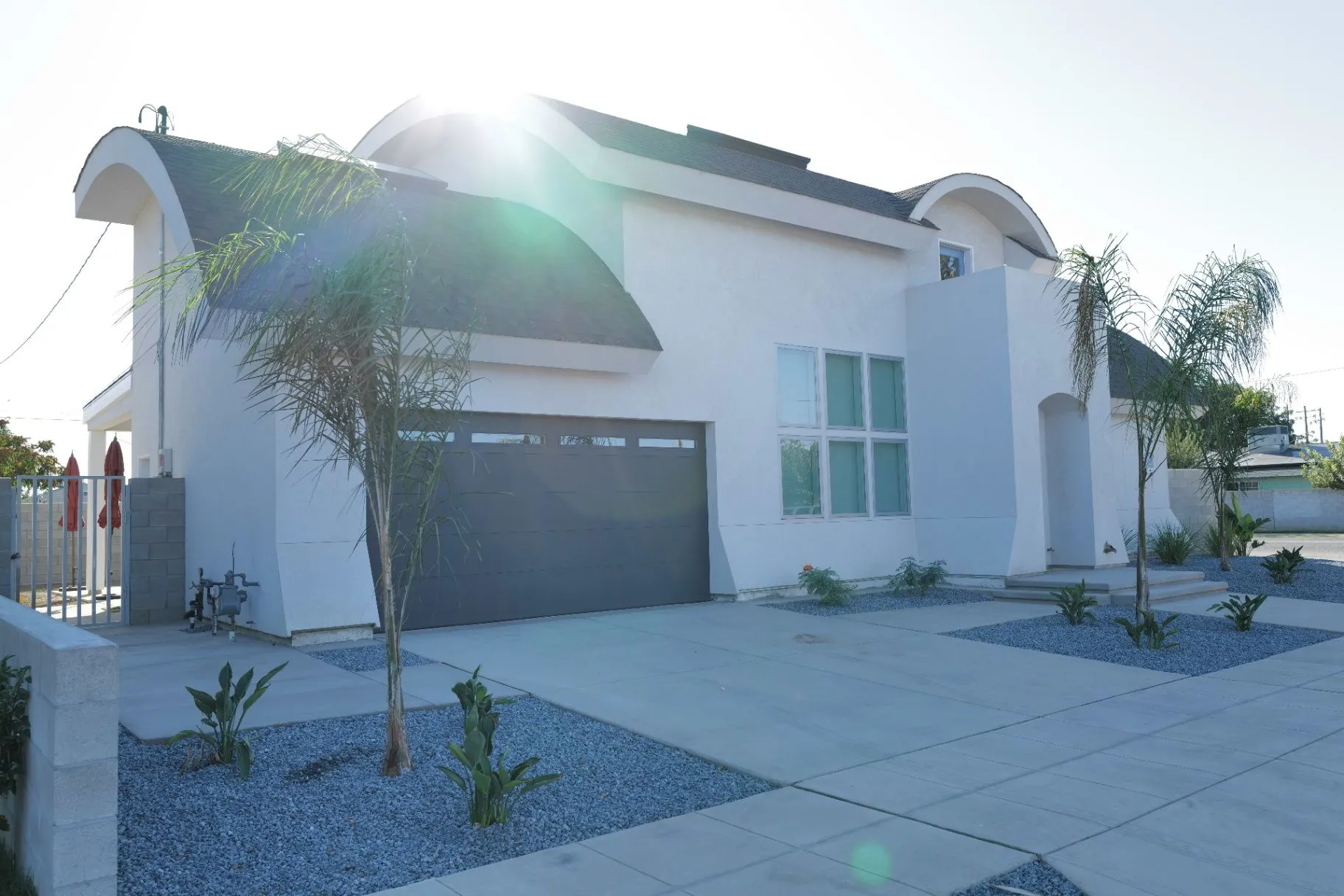 LOT14 HOUSE. White exterior with sweeping barrel and arched roofs, sun flare, and dark garage door.