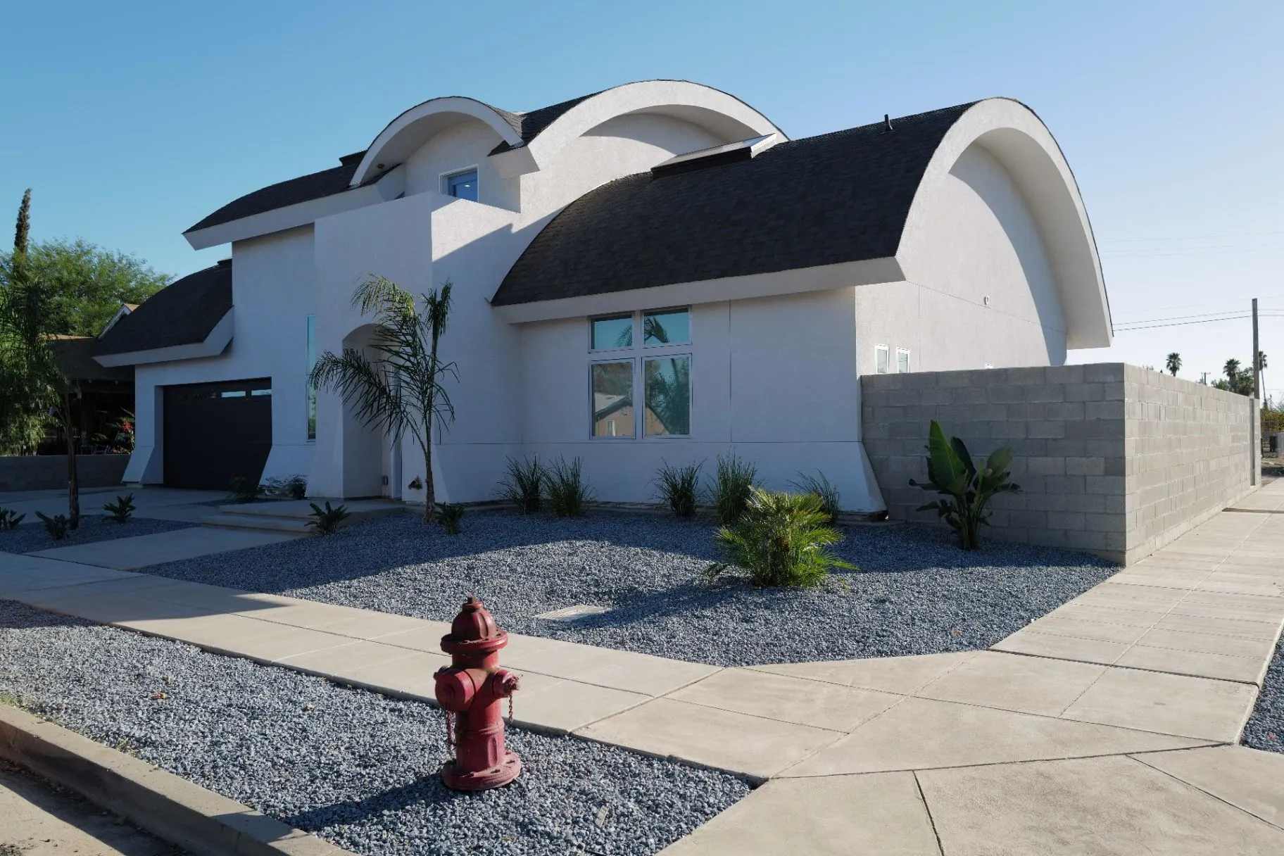 LOT14 HOUSE. White exterior with sweeping barrel roofs and a red fire hydrant in the gravel forecourt.