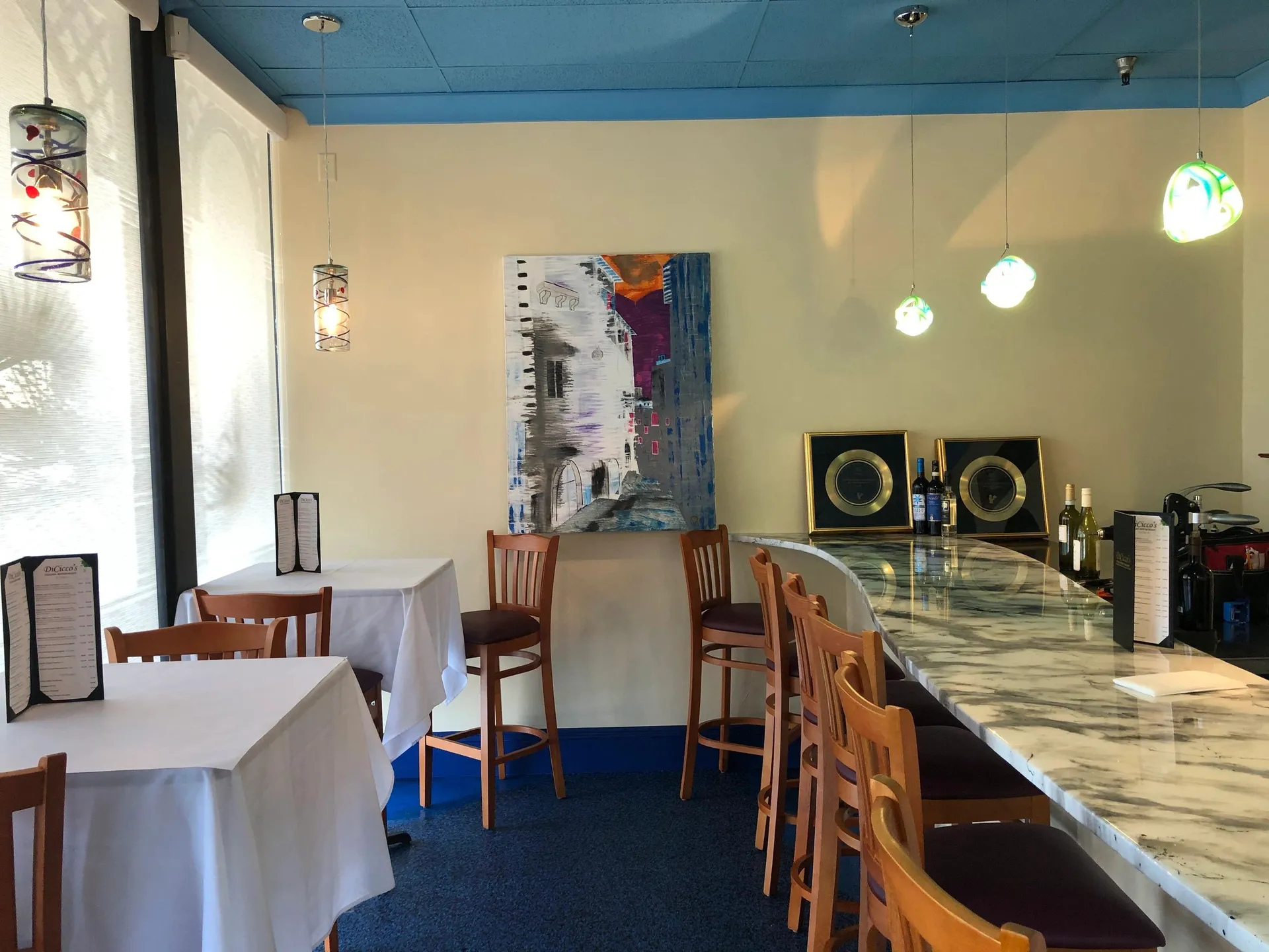DICICCO'S ITALIAN RESTAURANT. Wine bar with a curved counter, tables, a painting by the owner on the wall, and blue ceiling.